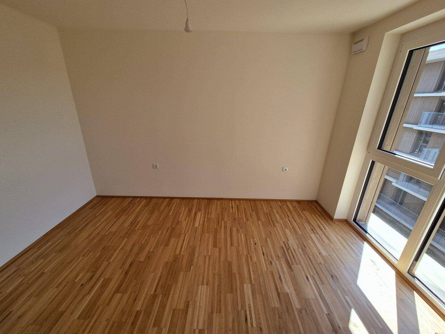Geräumiges Zimmer mit Holzparkettboden und großen Fenstern, die viel Licht spenden.
