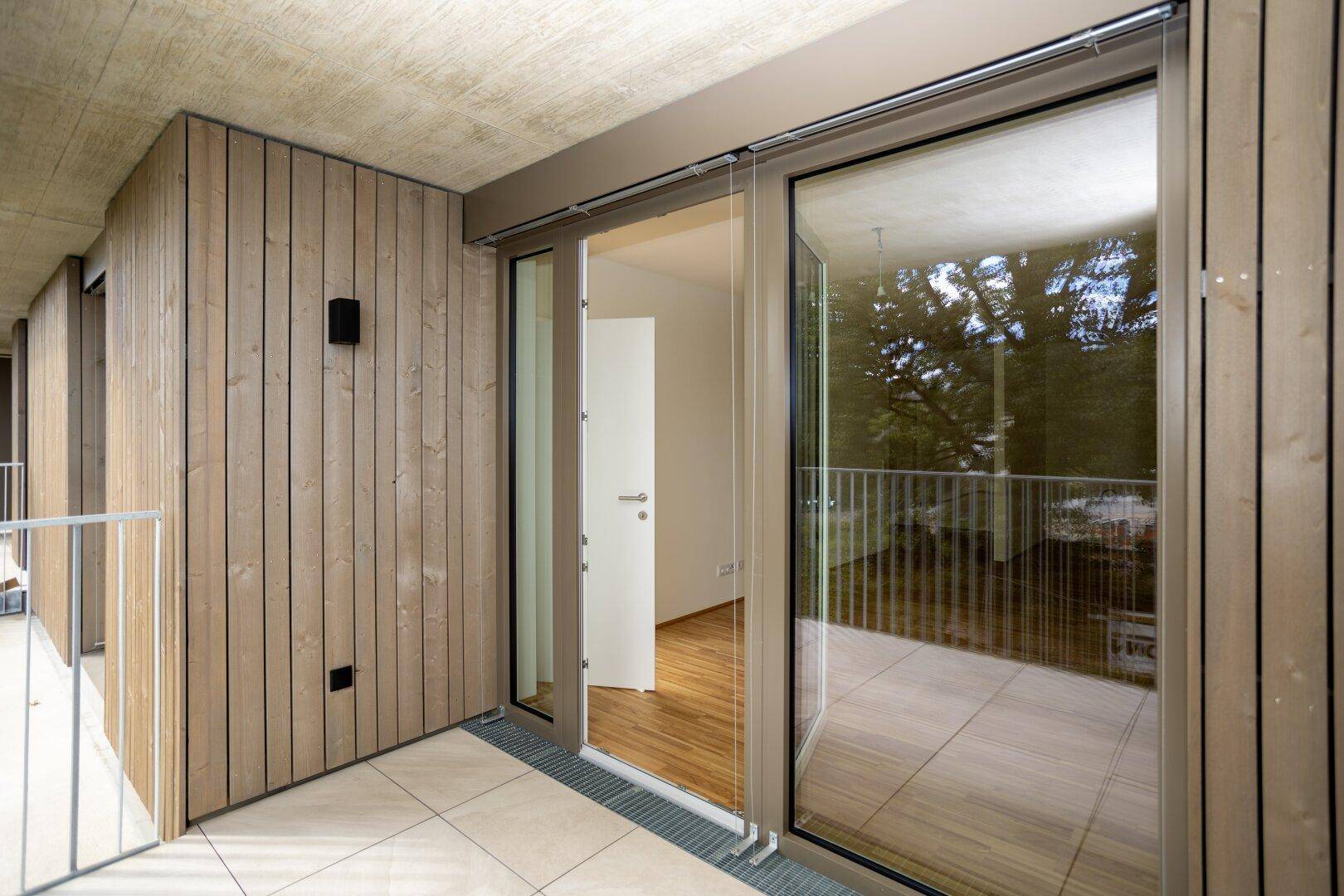 Geräumiger Balkon mit Holzverkleidung, Fliesenboden und Zugang zu einem hellen Innenraum.