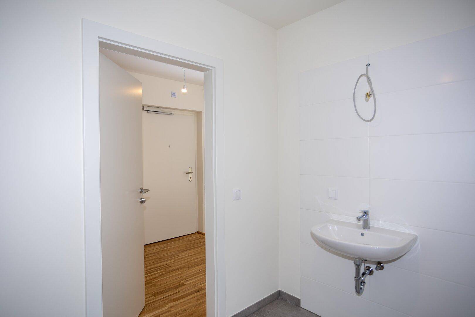 Helles Badezimmer mit Waschbecken, weißen Fliesen und Zugang zu einem weiteren Raum.