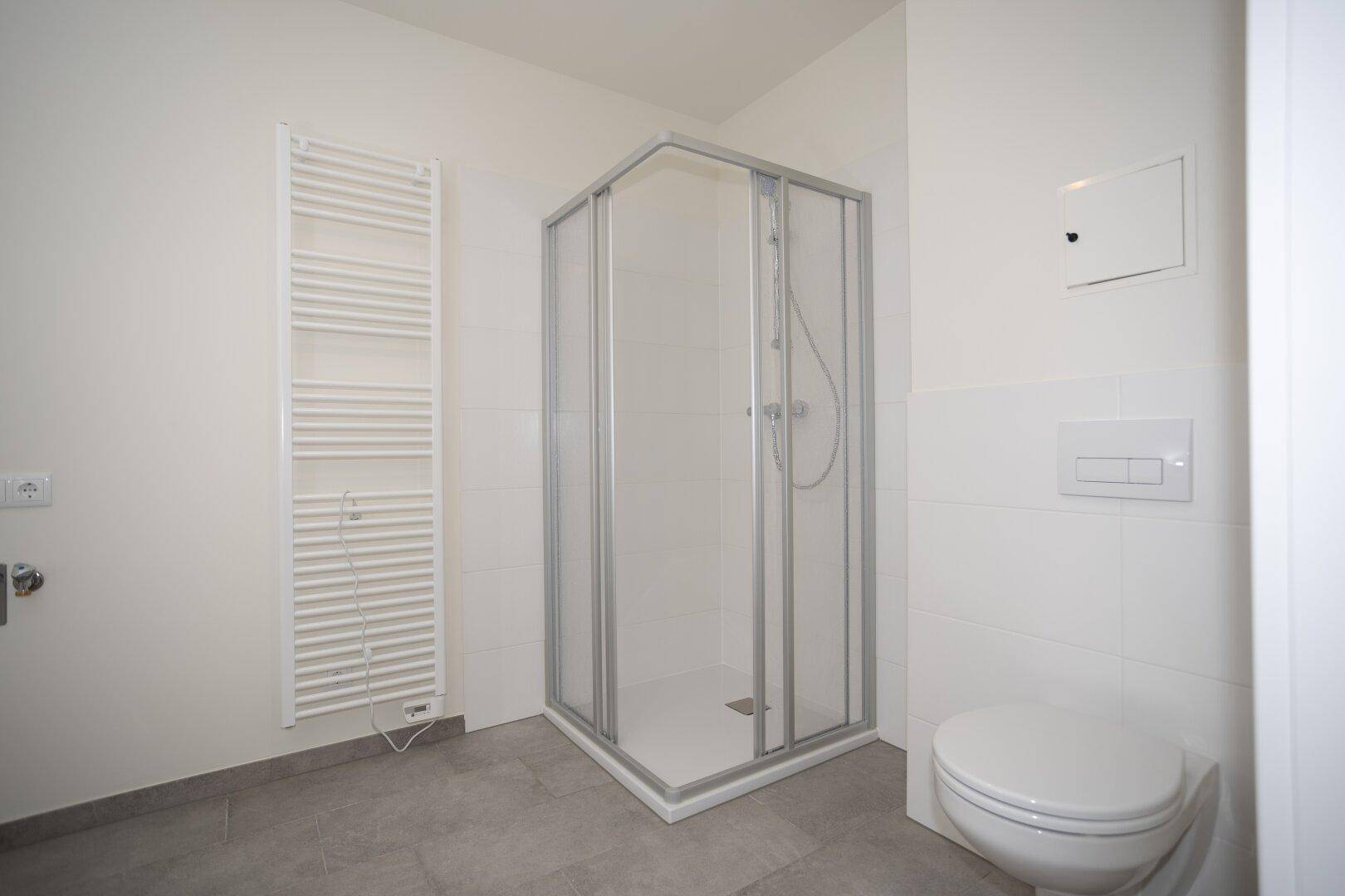 Modernes Badezimmer mit Duschkabine, wandhängendem WC und praktischem Handtuchheizkörper.