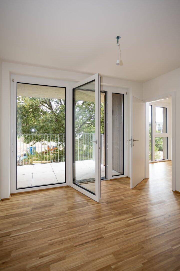 Heller Raum mit Parkettboden und großen Fenstertüren, die viel Tageslicht hereinlassen.