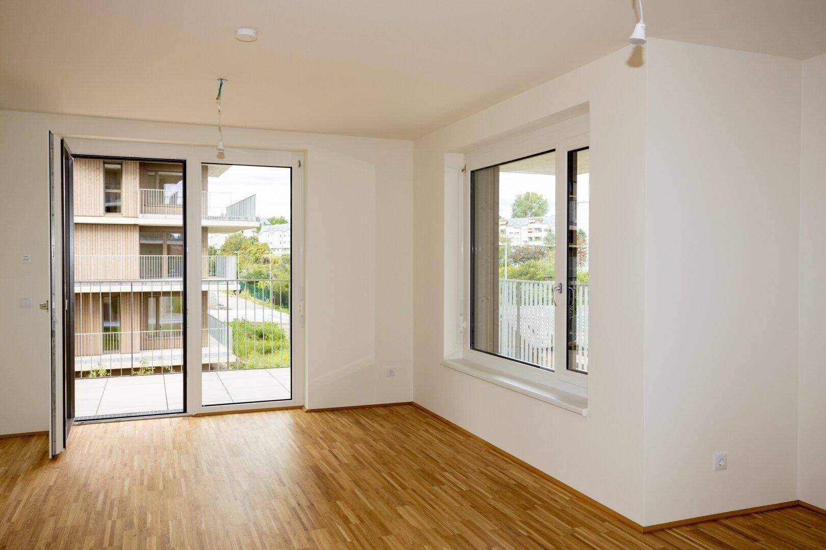 Helles Wohnzimmer mit Parkettboden, großen Fenstern und Zugang zu einem Balkon.