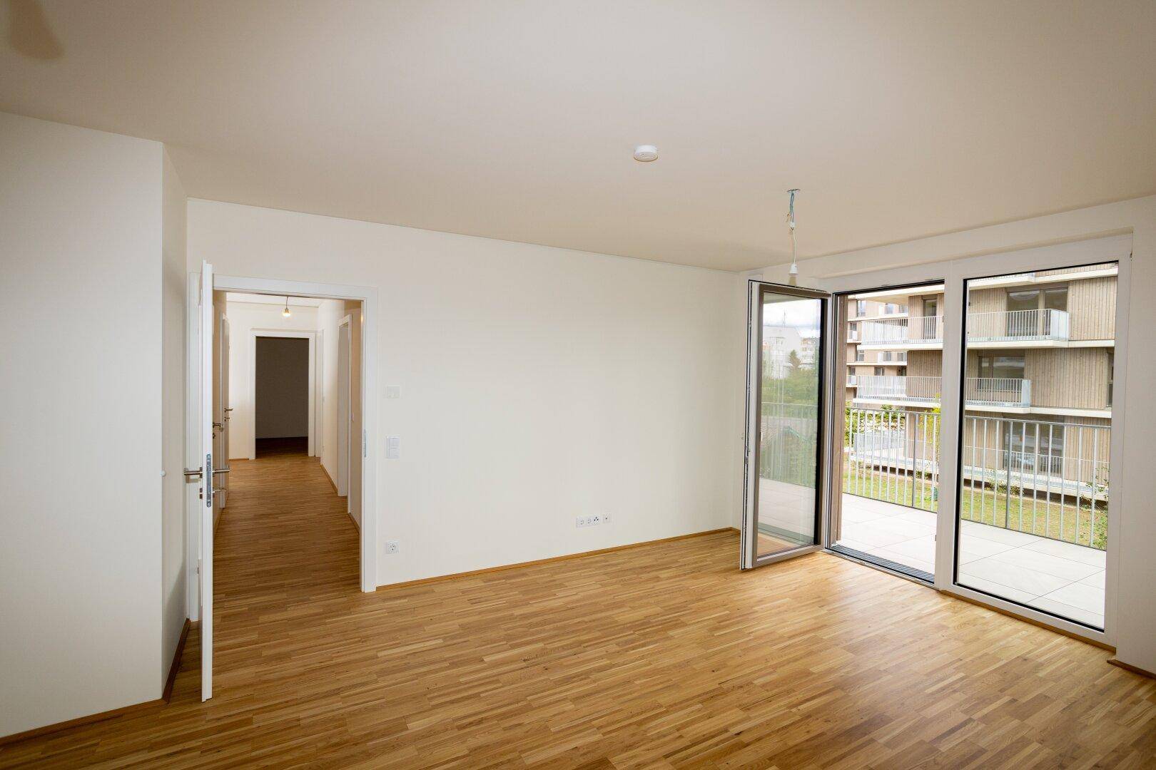 Geräumiges Wohnzimmer mit Parkettboden und offenem Zugang zu einem Flur.