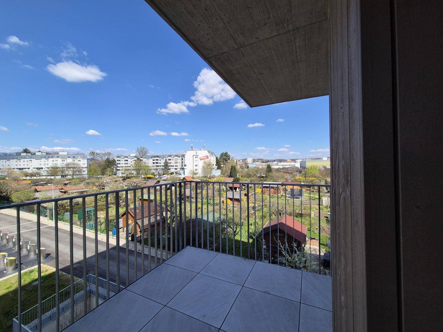 Balkon mit Fliesenboden und weitem Blick über Kleingärten und die städtische Umgebung.