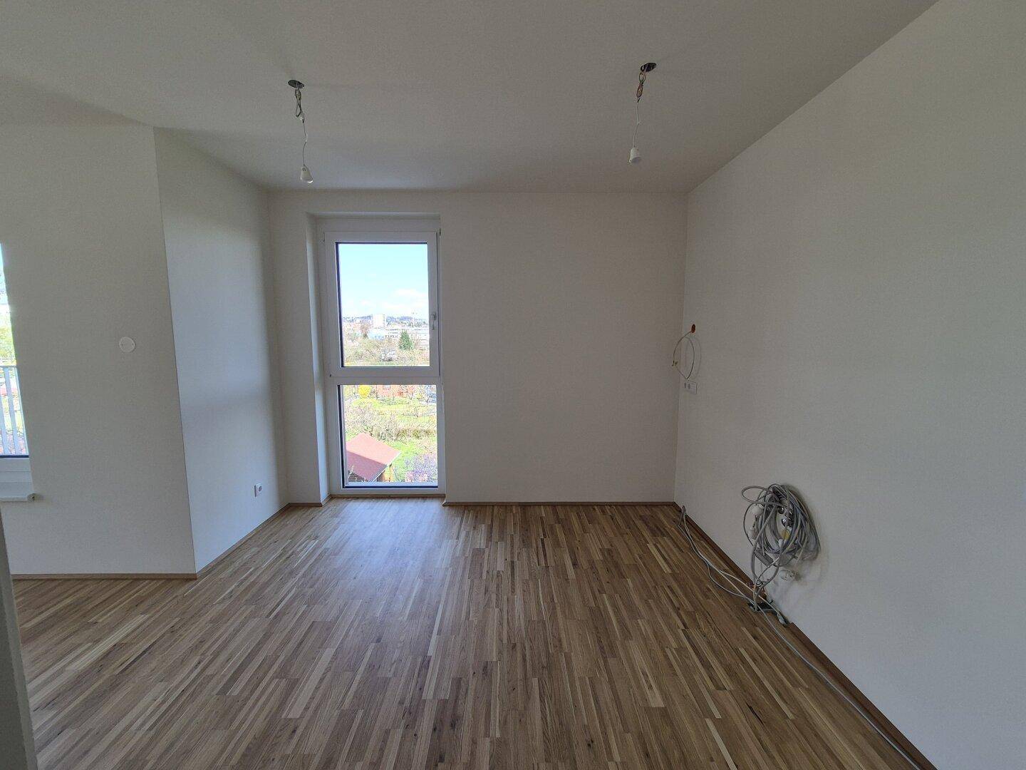 Heller Raum mit Parkettboden und Fenster, das einen Blick ins Grüne bietet.