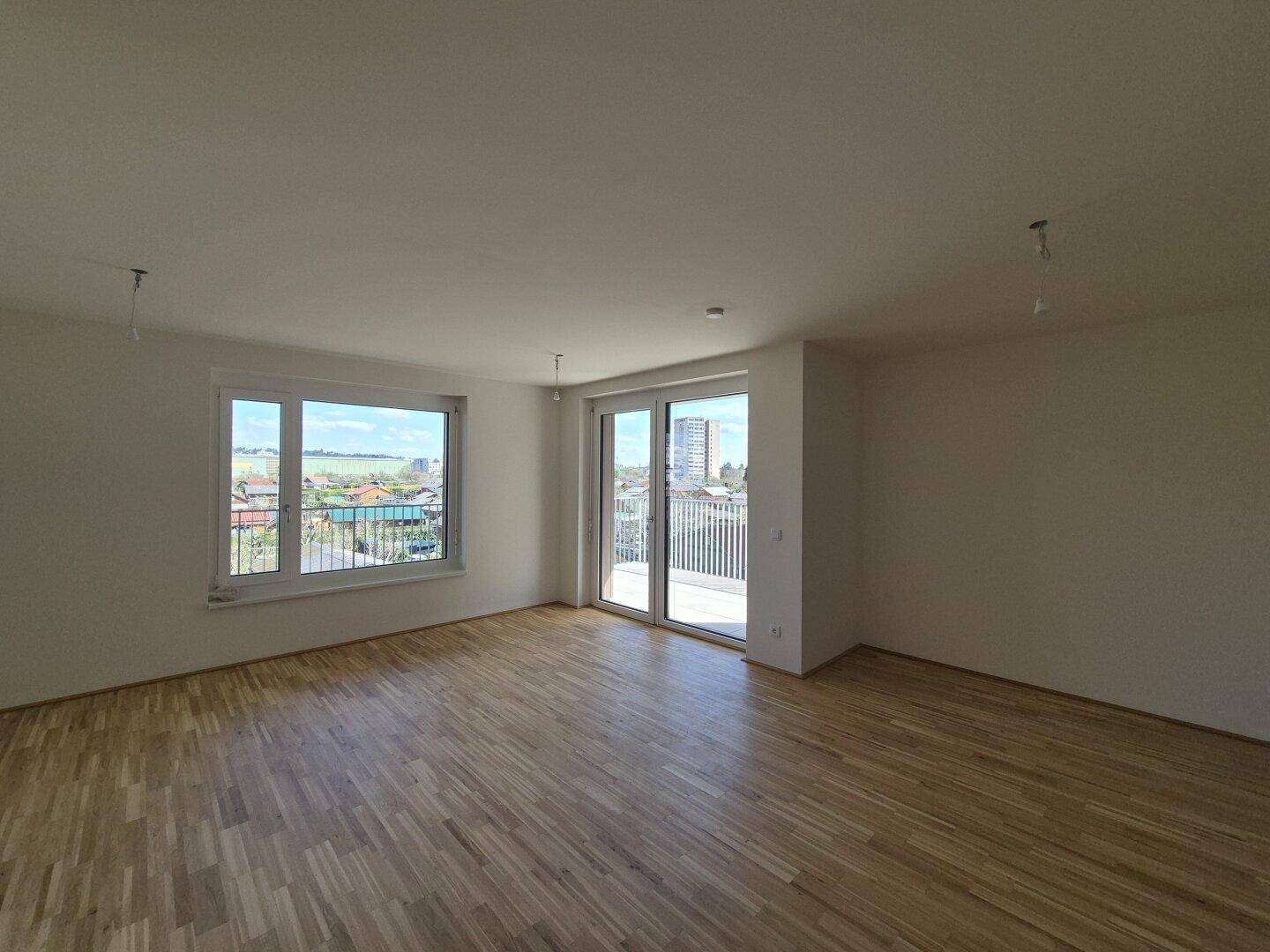 Geräumiges Wohnzimmer mit Parkettboden, großen Fenstern und Balkonzugang mit Stadtblick.