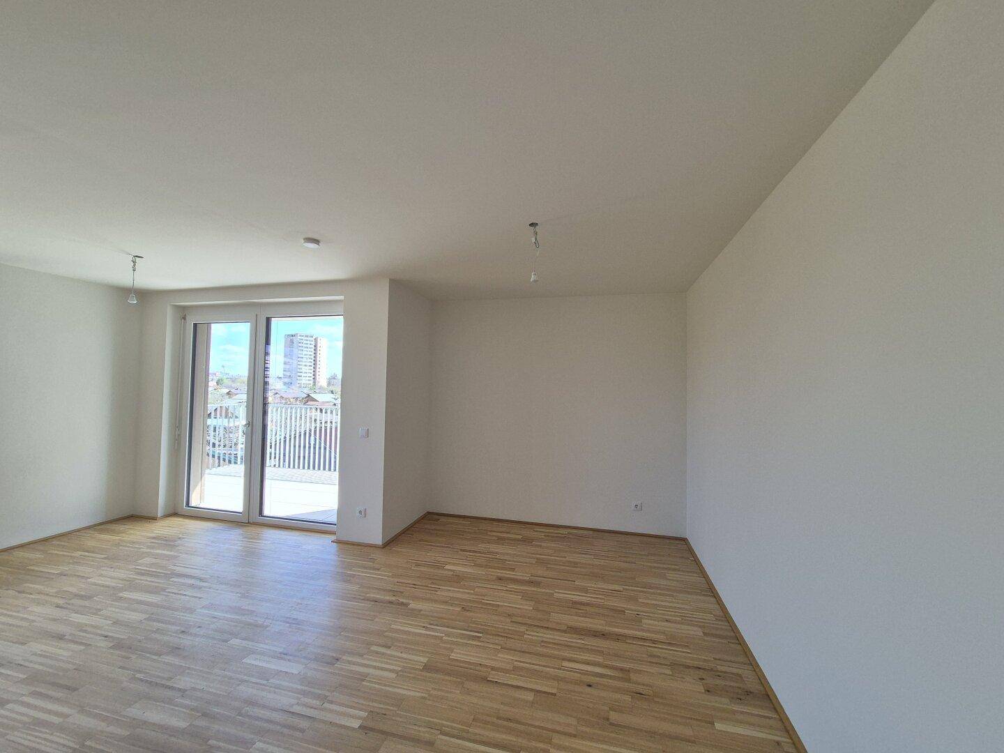 Helles Wohnzimmer mit Parkettboden und Zugang zum Balkon, bereit für individuelle Gestaltung.
