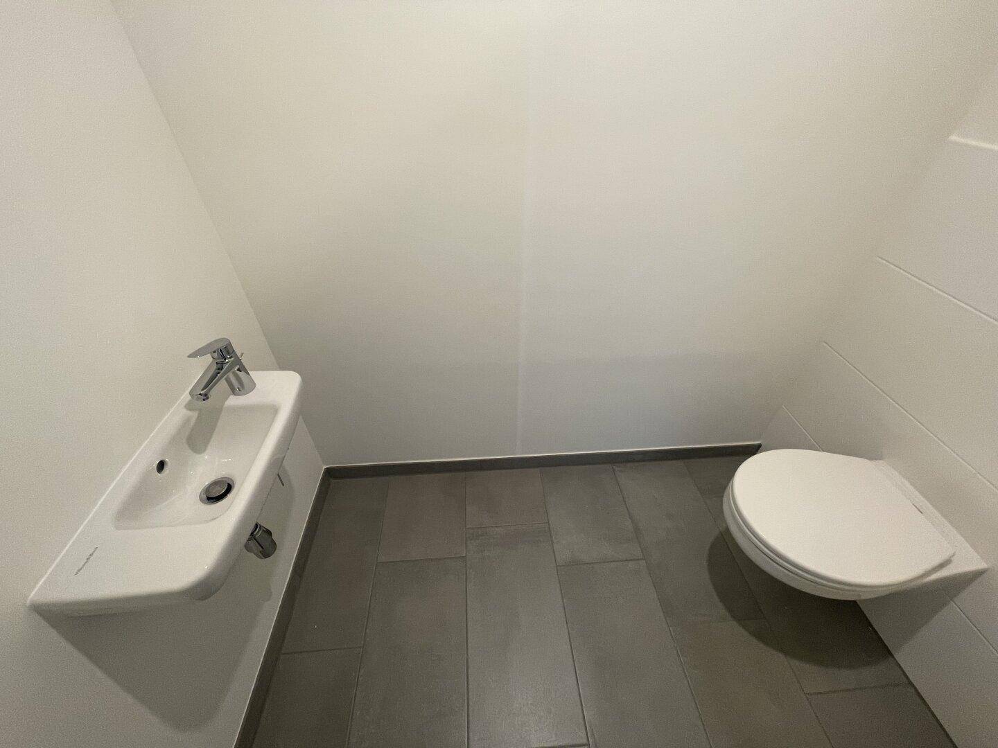 Modernes Gäste-WC mit Wand-WC und kleinem Waschbecken, ausgestattet mit Fliesenboden.
