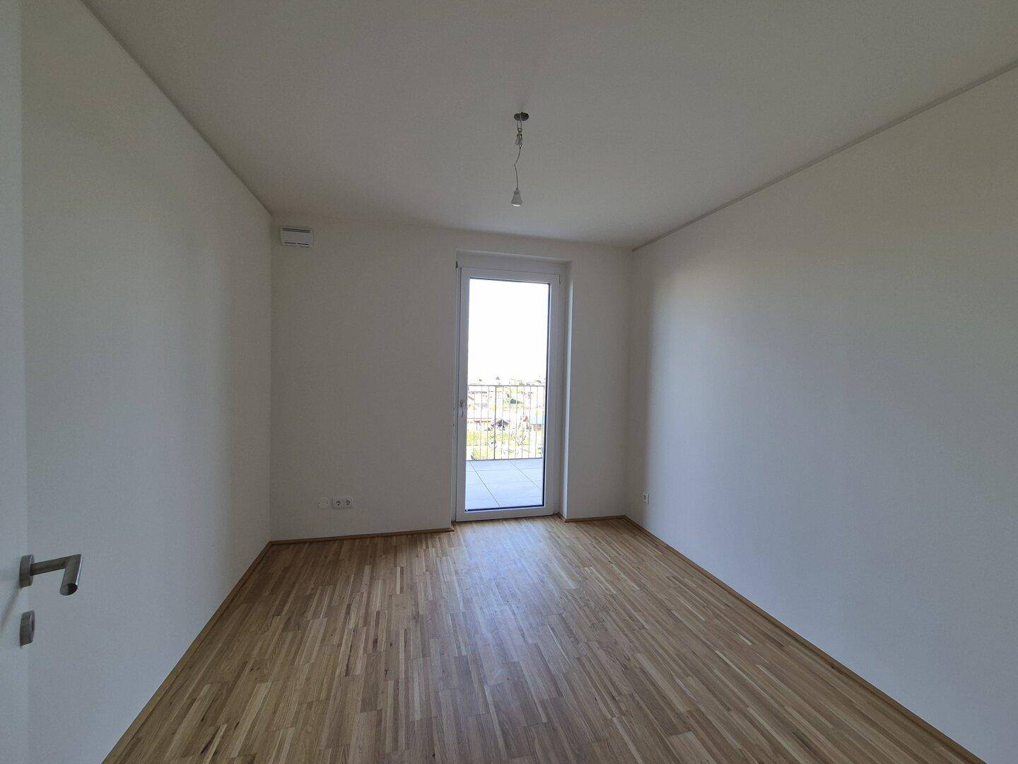Helles Schlafzimmer mit Parkettboden und Zugang zu einem kleinen Balkon.