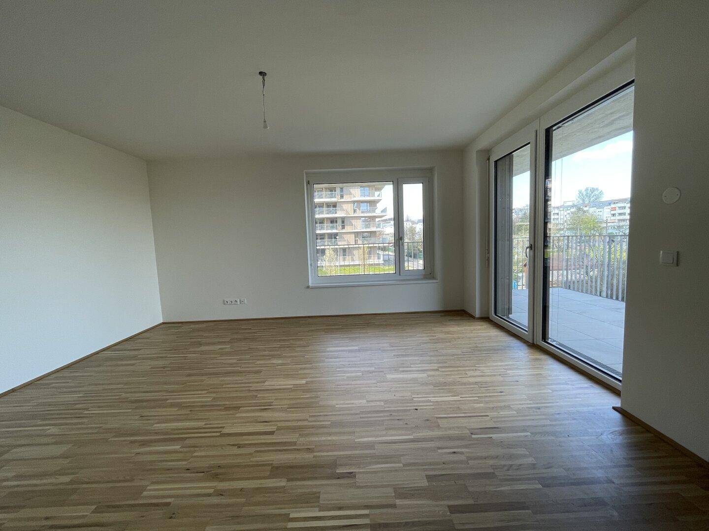 Geräumiges Wohnzimmer mit Parkettboden und großen Fenstern, die Zugang zu einem Balkon bieten.