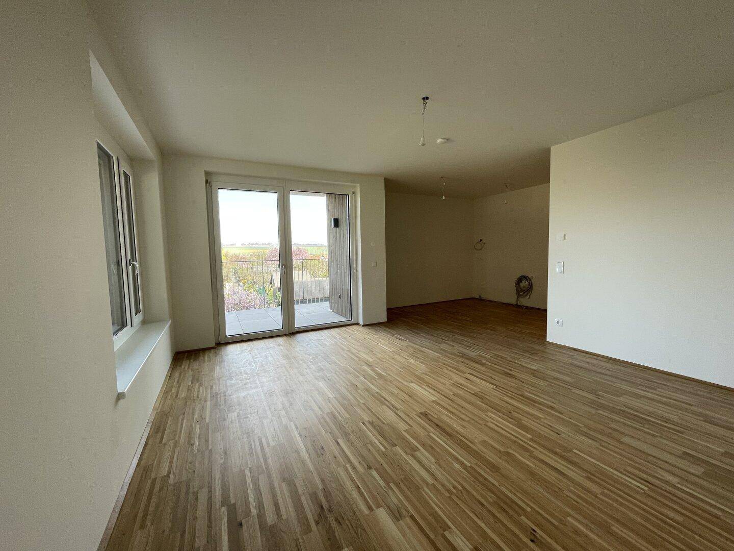 Helles Wohnzimmer mit Parkettboden und Zugang zum Balkon, ideal für entspannte Stunden mit Ausblick.