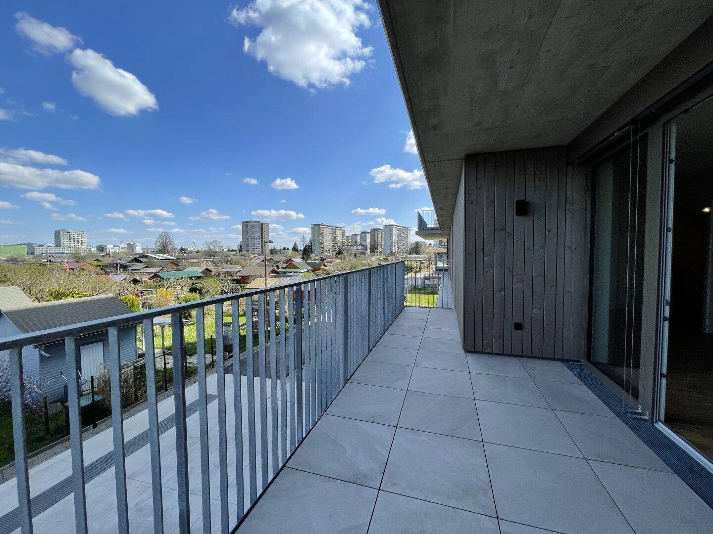 Moderner Balkon mit Fliesenboden und Holzverkleidung, bietet einen weiten Blick über die Stadtlandschaft.
