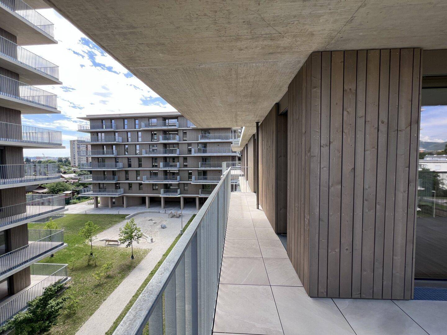 Geräumiger Balkon mit Fliesenboden und weitem Blick auf die moderne Wohnanlage und Grünflächen.