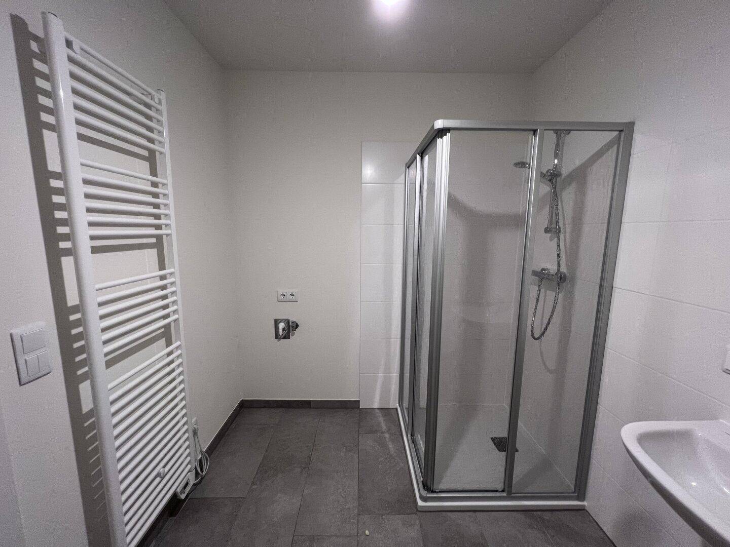 Funktionales Badezimmer mit Duschkabine, Waschbecken und praktischem Handtuchheizkörper.