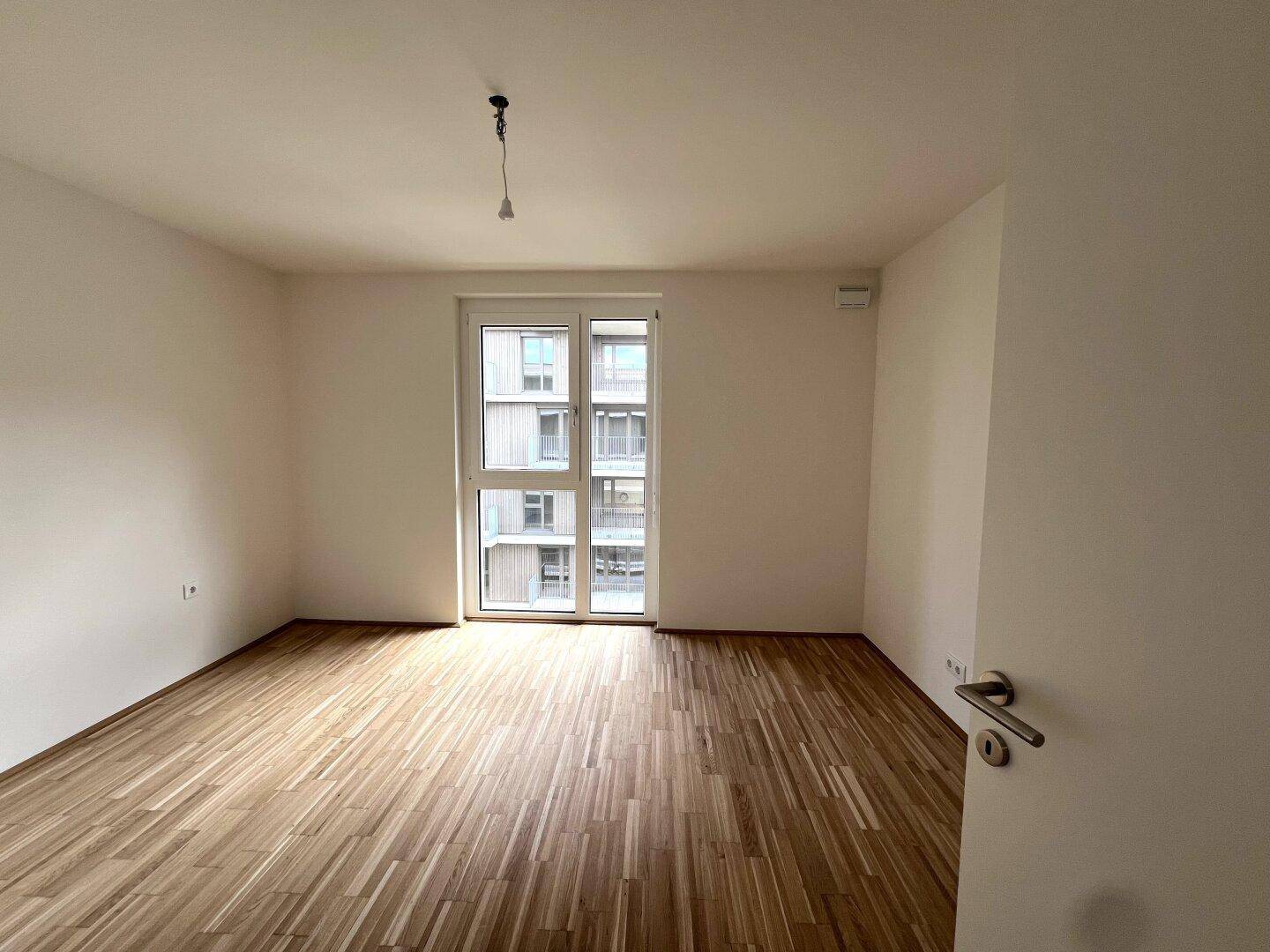 Helles Schlafzimmer mit Parkettboden und Zugang zu einem kleinen Außenbereich.