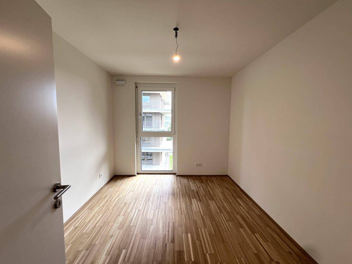 Geräumiges Schlafzimmer mit hellem Parkettboden und Fensterfront.
