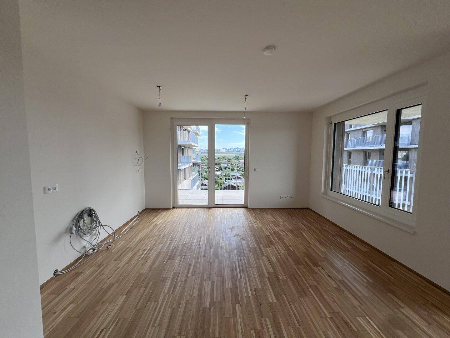 Heller Wohnraum mit Parkettboden, großen Fenstern und Zugang zu einem Balkon.