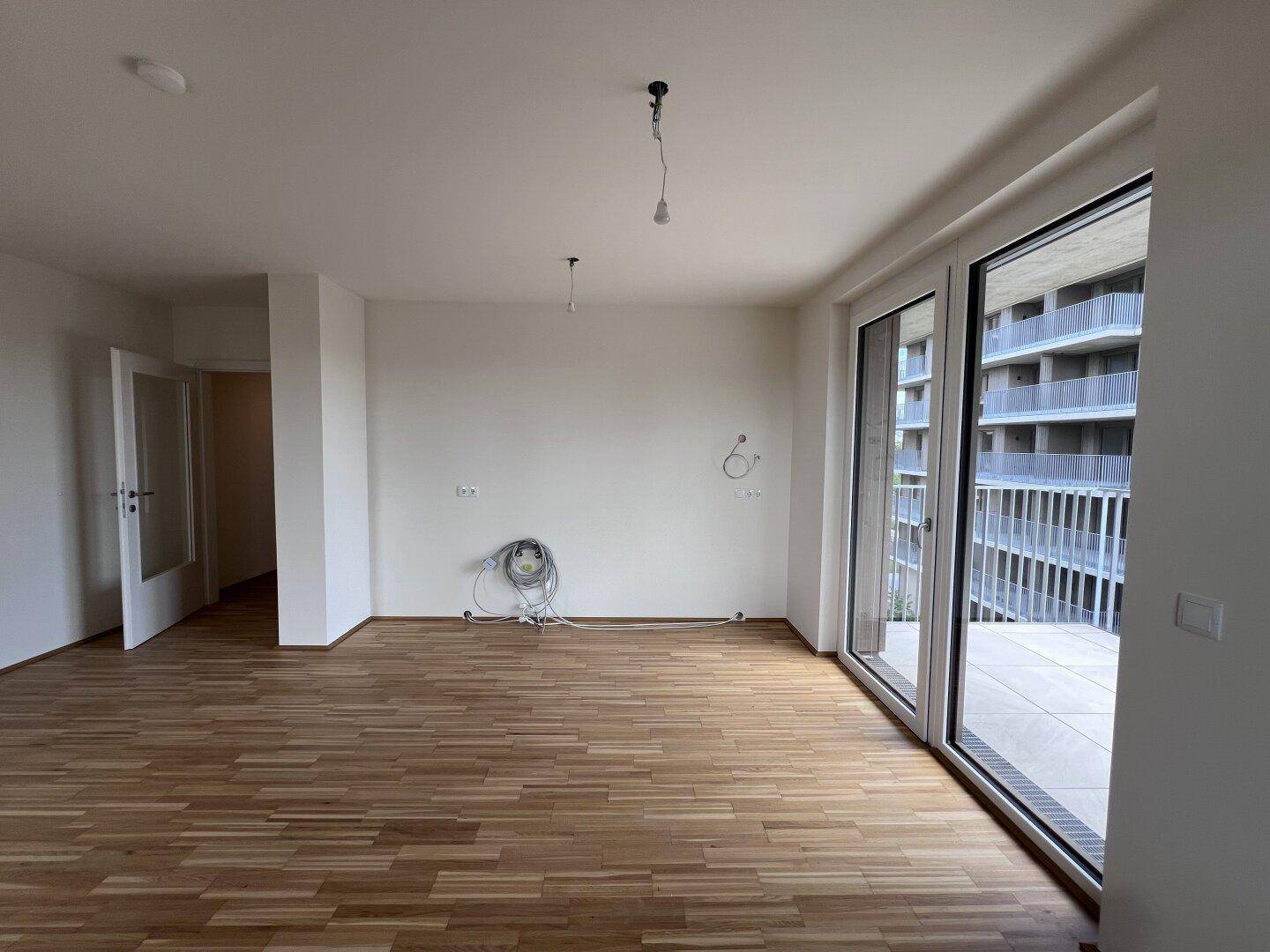Großer Wohnbereich mit Parkettboden und breiter Schiebetür zur Terrasse.