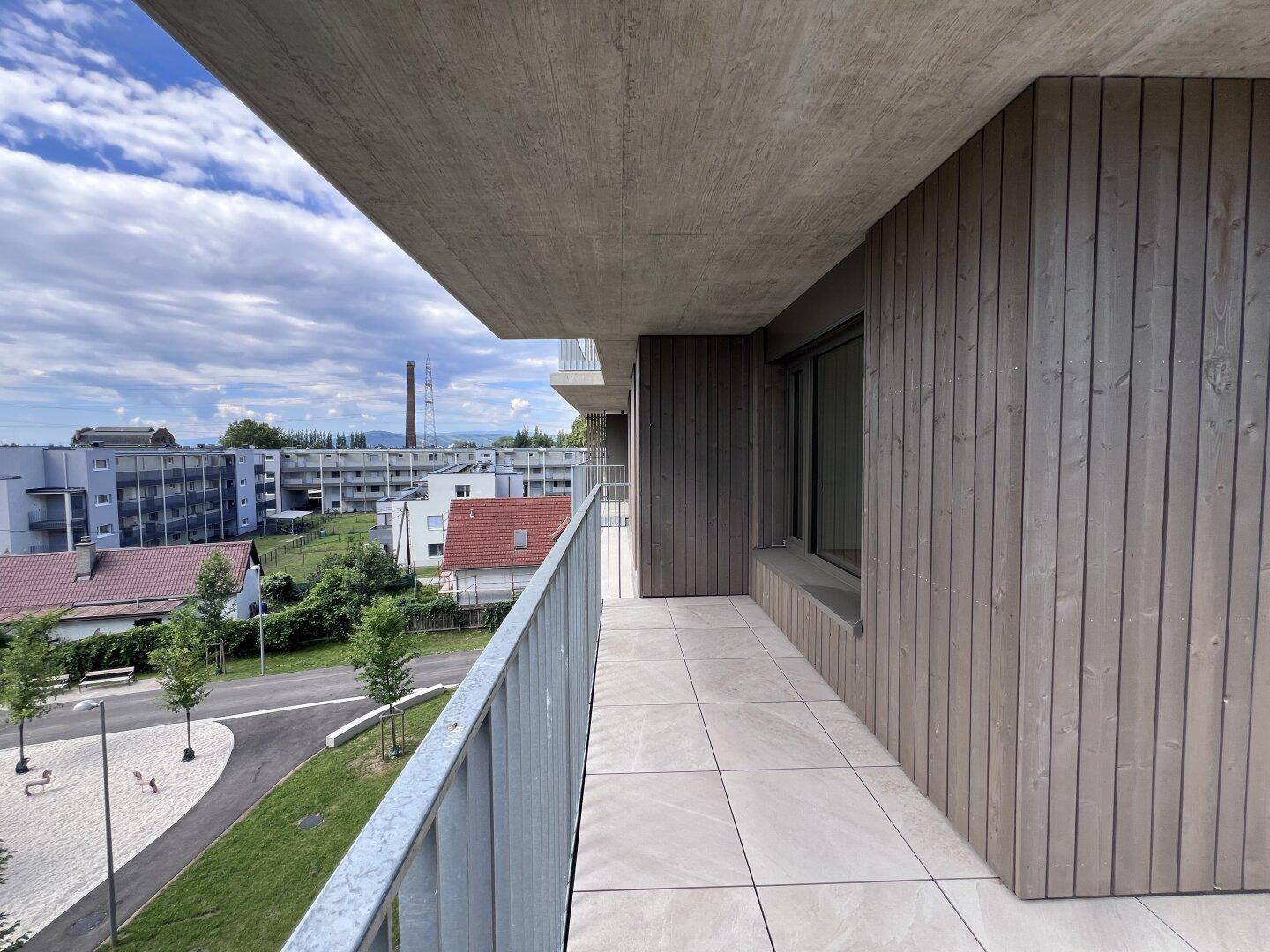 Geräumiger Balkon mit Holzfassade, Fliesenboden und Ausblick auf die Umgebung.