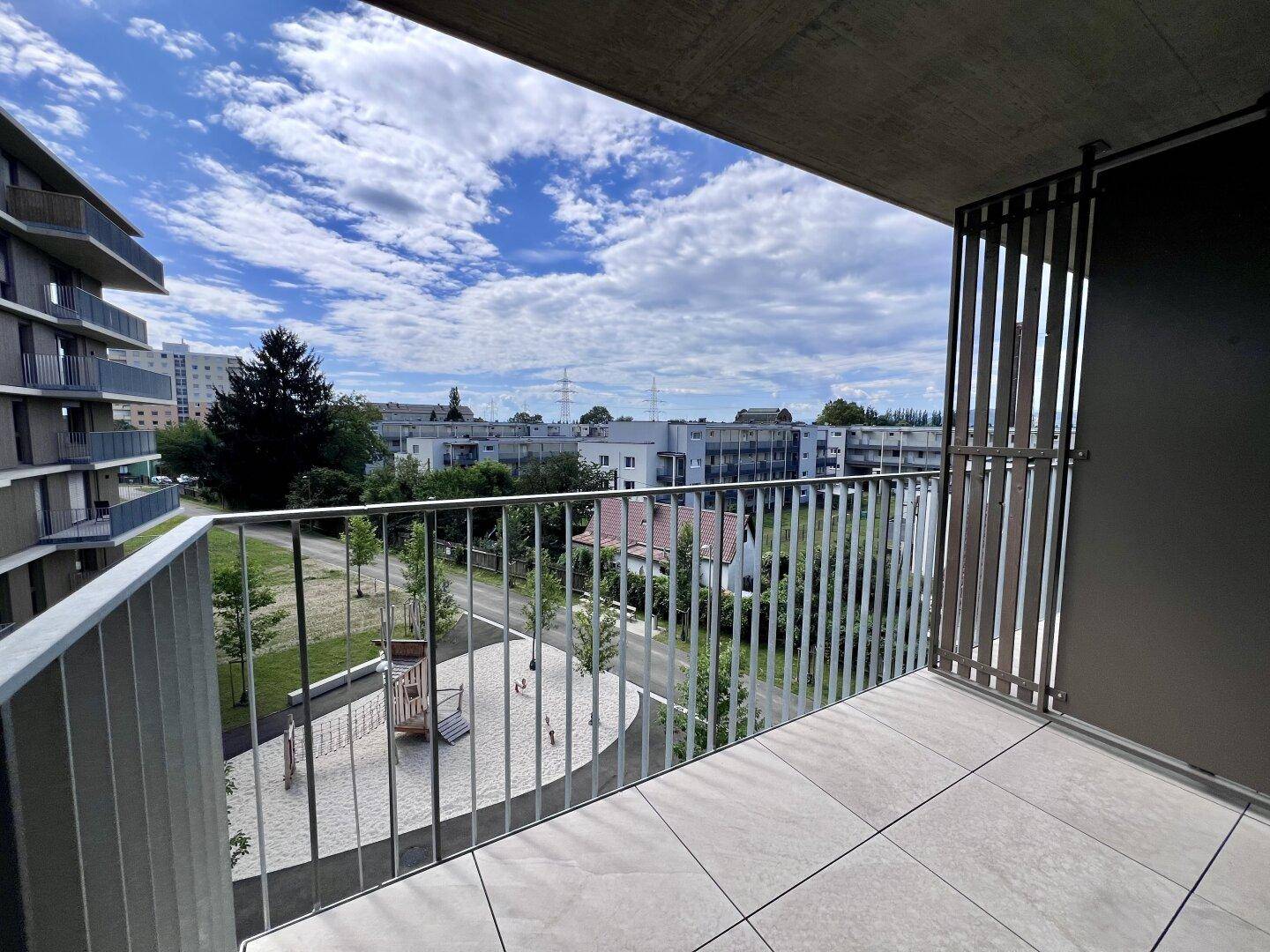 Heller Balkon mit Fliesen und Blick auf einen Spielplatz sowie die umliegende Wohnbebauung.
