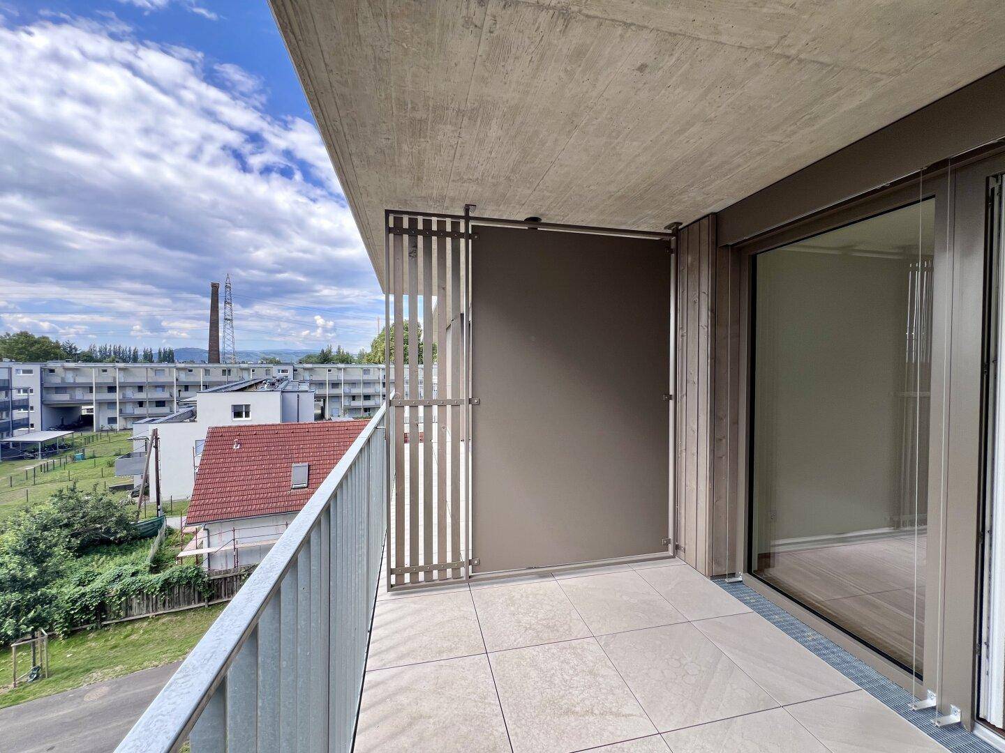 Moderner Balkon mit Fliesenboden und seitlichem Sichtschutz, bietet einen Blick auf die Landschaft.