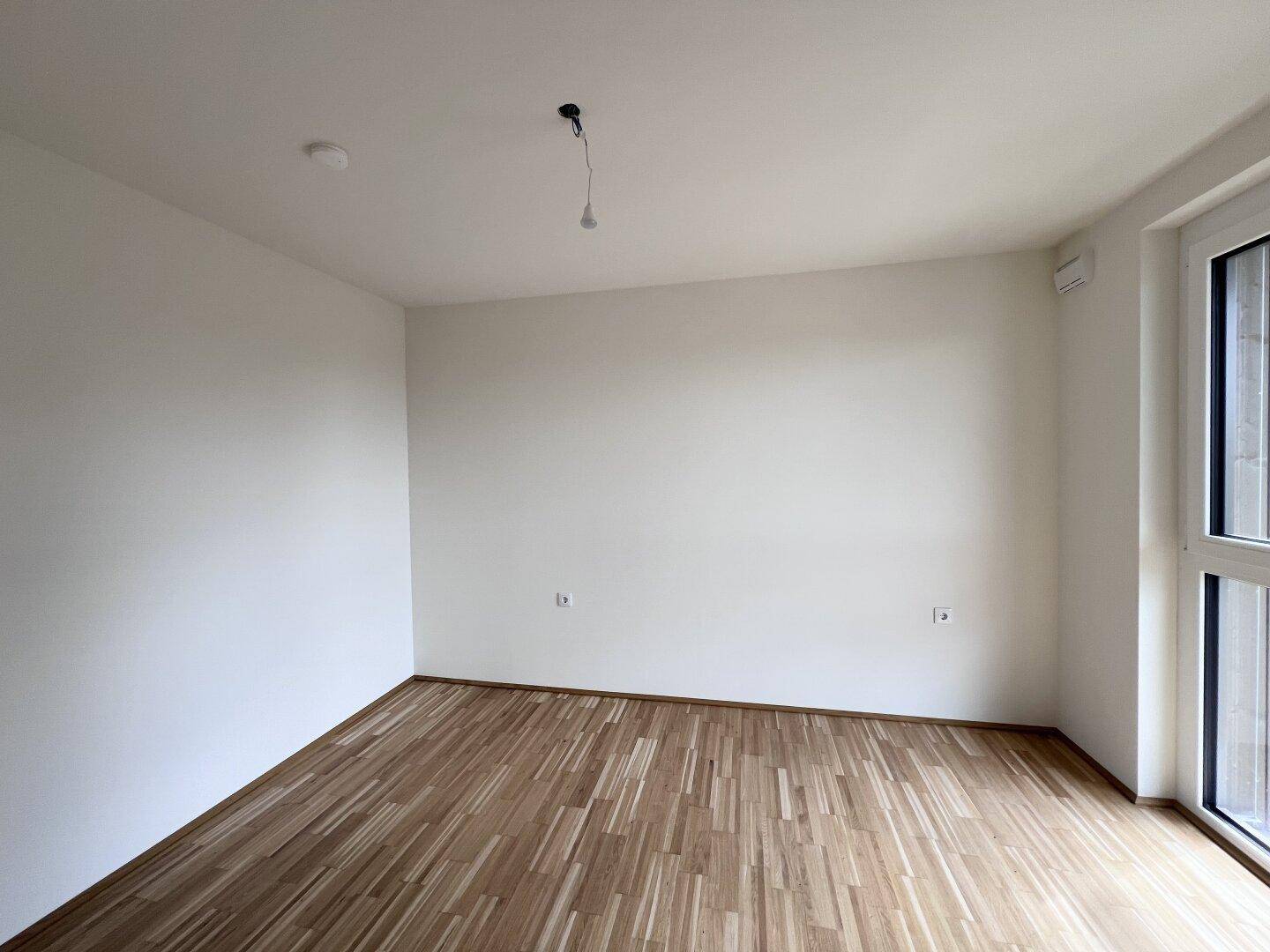 Leeres Schlafzimmer mit Parkettboden und weiß gestrichenen Wänden, bereit zur individuellen Gestaltung.