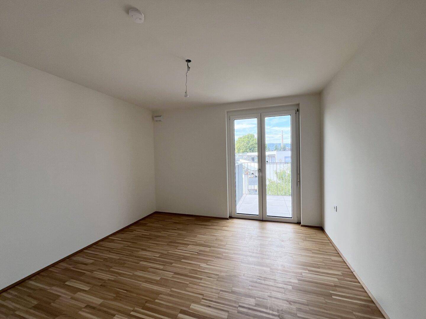 Leeres Zimmer mit Parkettboden und Balkontür, ideal als Schlaf- oder Arbeitszimmer, sehr hell.