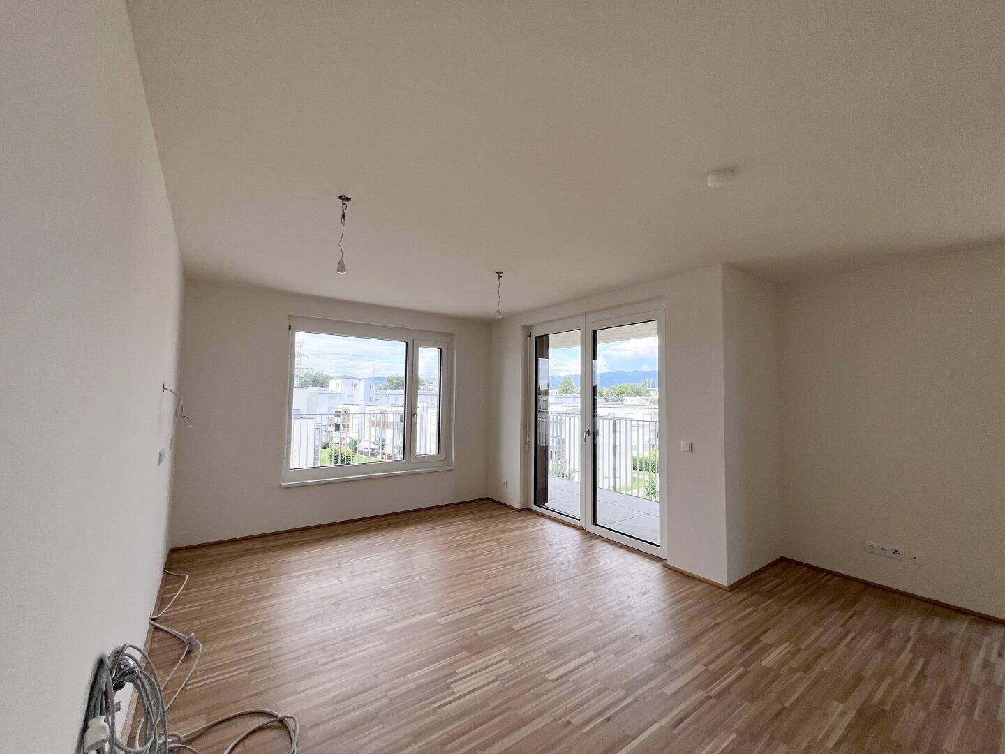 Geräumiges Wohnzimmer mit Parkettboden, großen Fenstern und Blick auf die Umgebung, lichtdurchflutet.