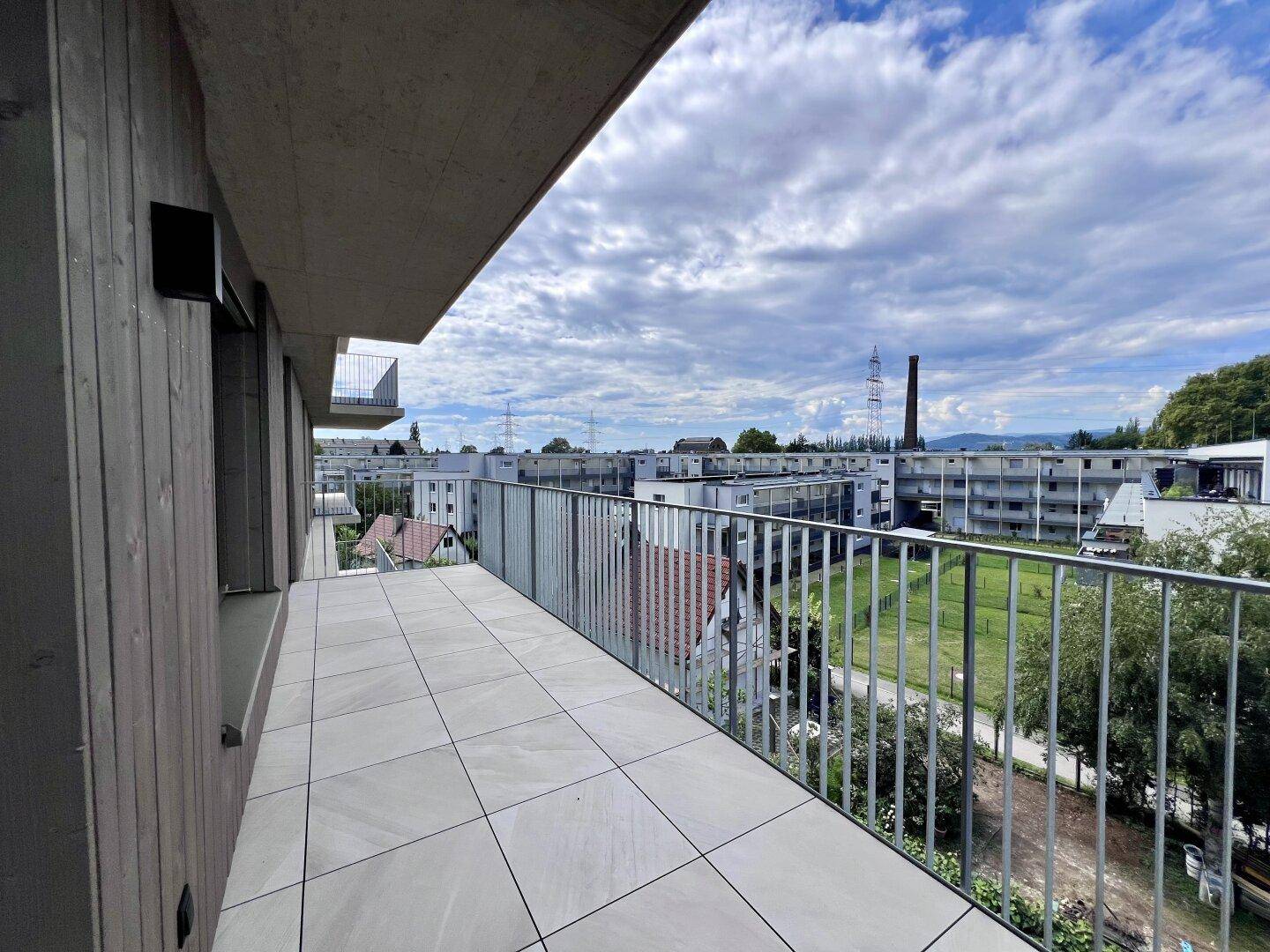 Geräumiger Balkon mit Fliesenboden und Metallgeländer, bietet weite Aussicht über die Umgebung.