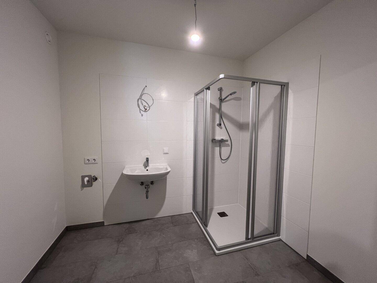 Modernes Badezimmer mit Duschkabine, Waschbecken und dunklen Fliesen, funktional und hell.