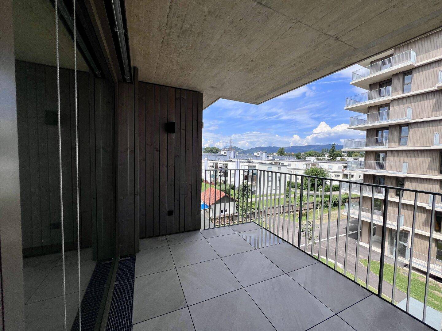 Moderner Balkon mit Fliesenboden und Metallgeländer, der einen Panoramablick auf die Stadt und Berge bietet.