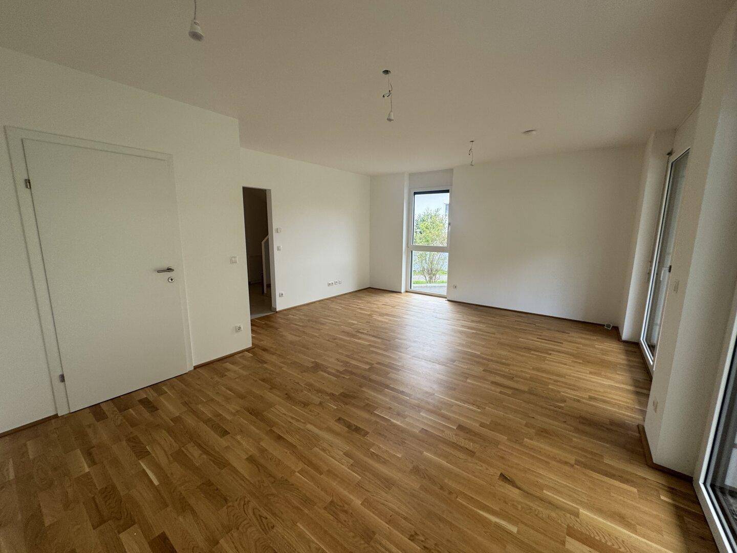 Geräumiges Wohnzimmer mit hellem Holzboden und großen Fenstern für viel Tageslicht.