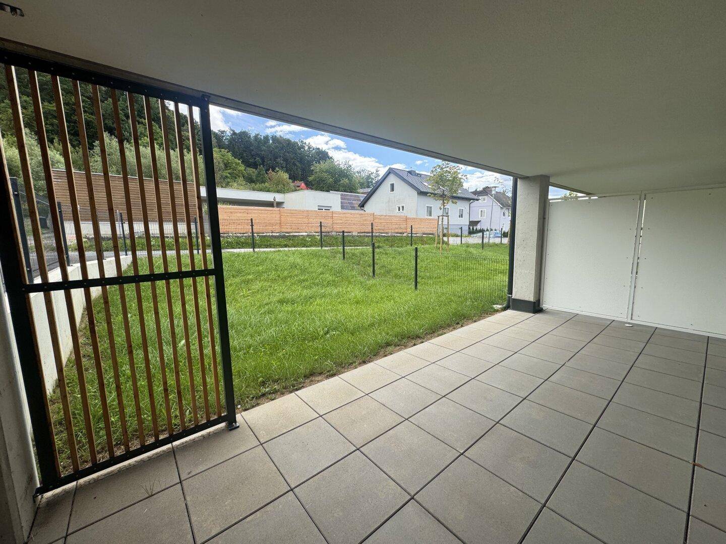 Überdachte Terrasse mit Fliesenboden und Blick auf den privaten Gartenbereich.