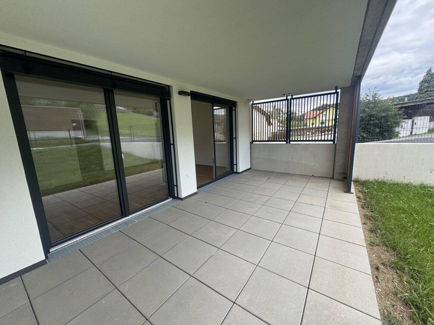Geräumige, überdachte Terrasse mit Fliesenboden und großen Glasschiebetüren zum Innenbereich.