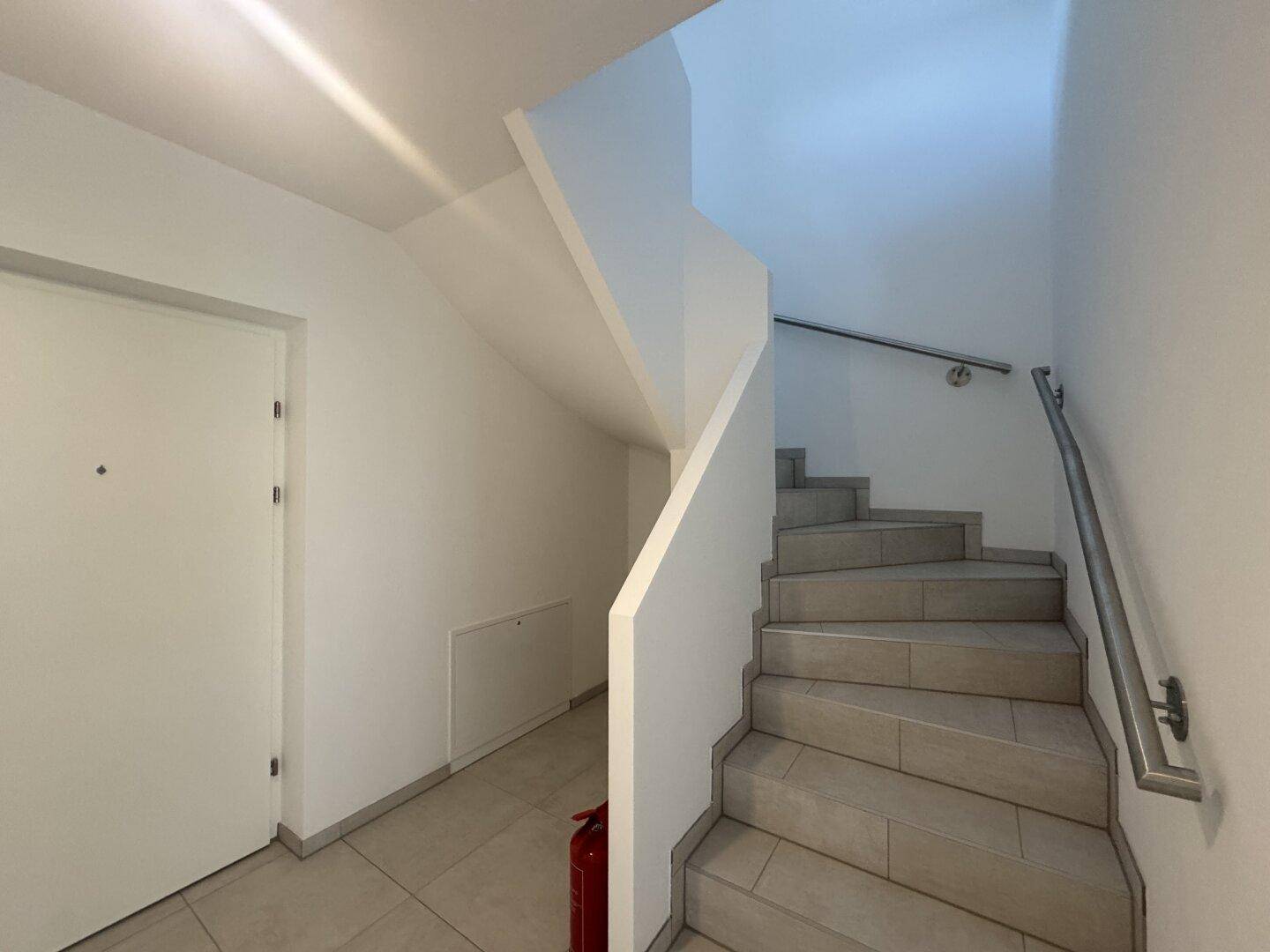 Heller Treppenaufgang mit Fliesenstufen und modernem Geländer in einem Mehrfamilienhaus.
