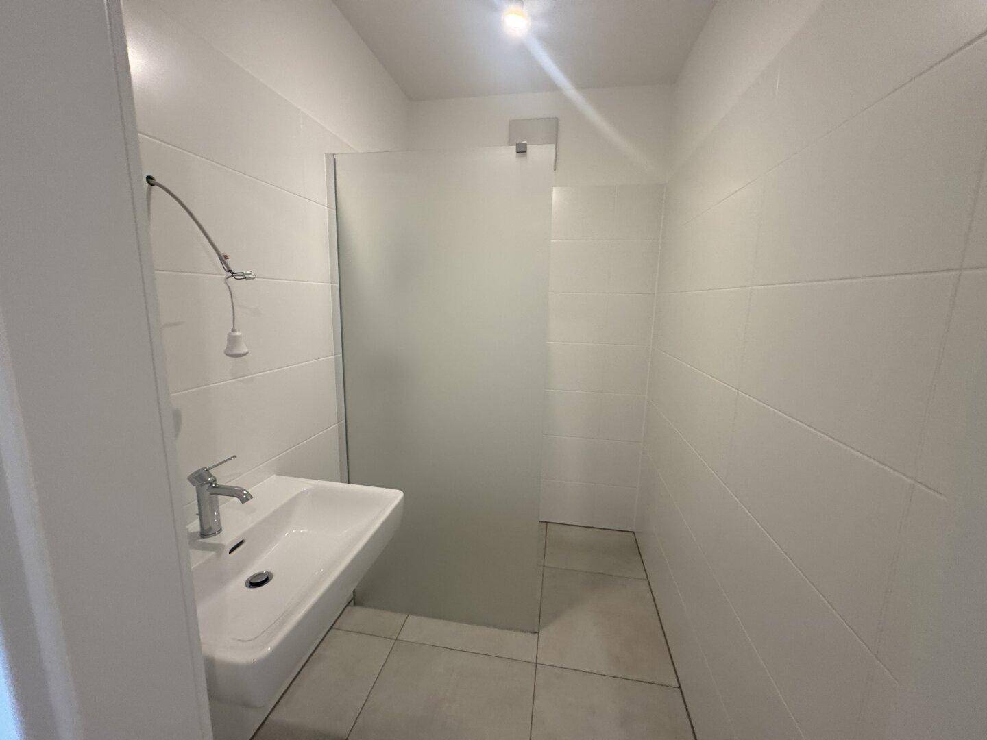 Modernes Badezimmer mit weiß gefliesten Wänden, Waschbecken und ebenerdiger Dusche.