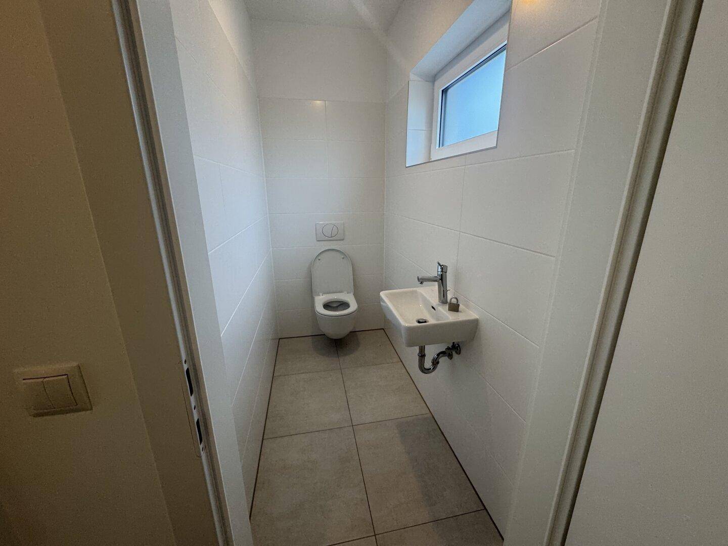Helles Gäste-WC mit Fenster, wandhängendem WC und kleinem Waschbecken.