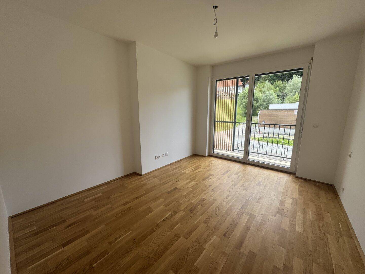 Schlafzimmer mit Holzboden und großem Fenster mit französischem Balkon und Blick ins Grüne.