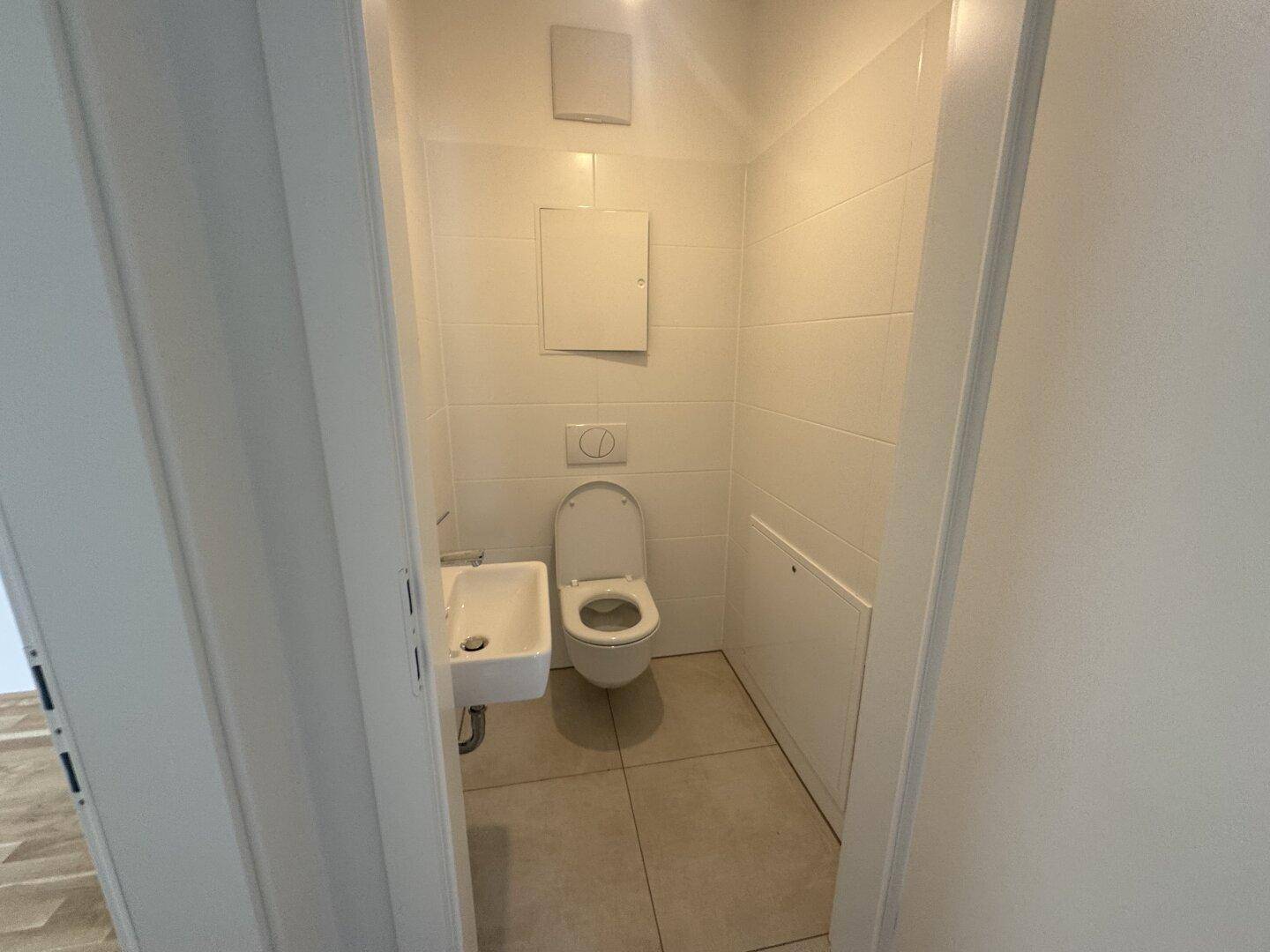Modernes Gäste-WC mit wandhängendem WC, kleinem Waschbecken und weißen Fliesen.