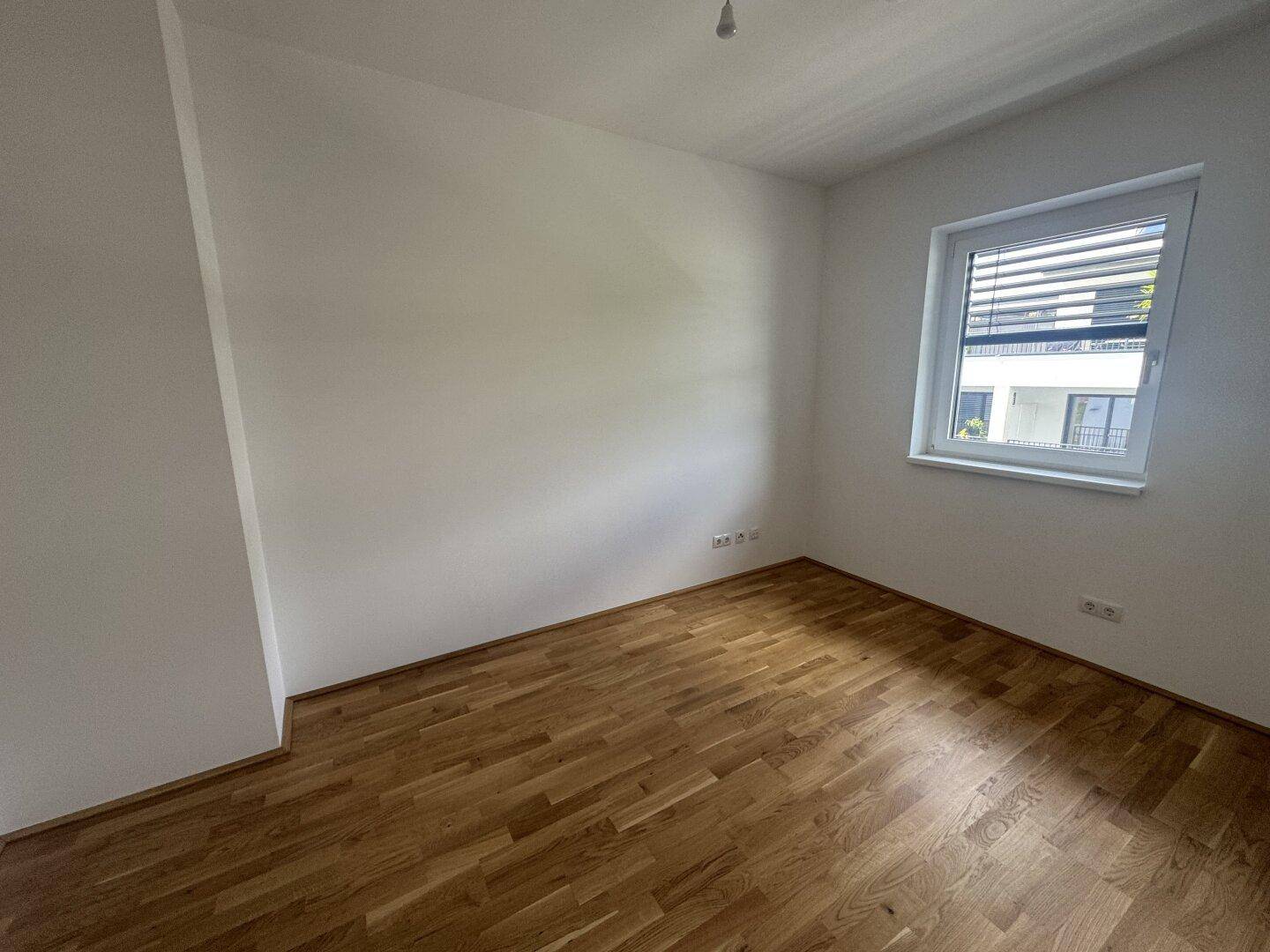 Geräumiges Schlafzimmer mit Holzboden und einem Fenster, das viel Tageslicht hereinlässt.