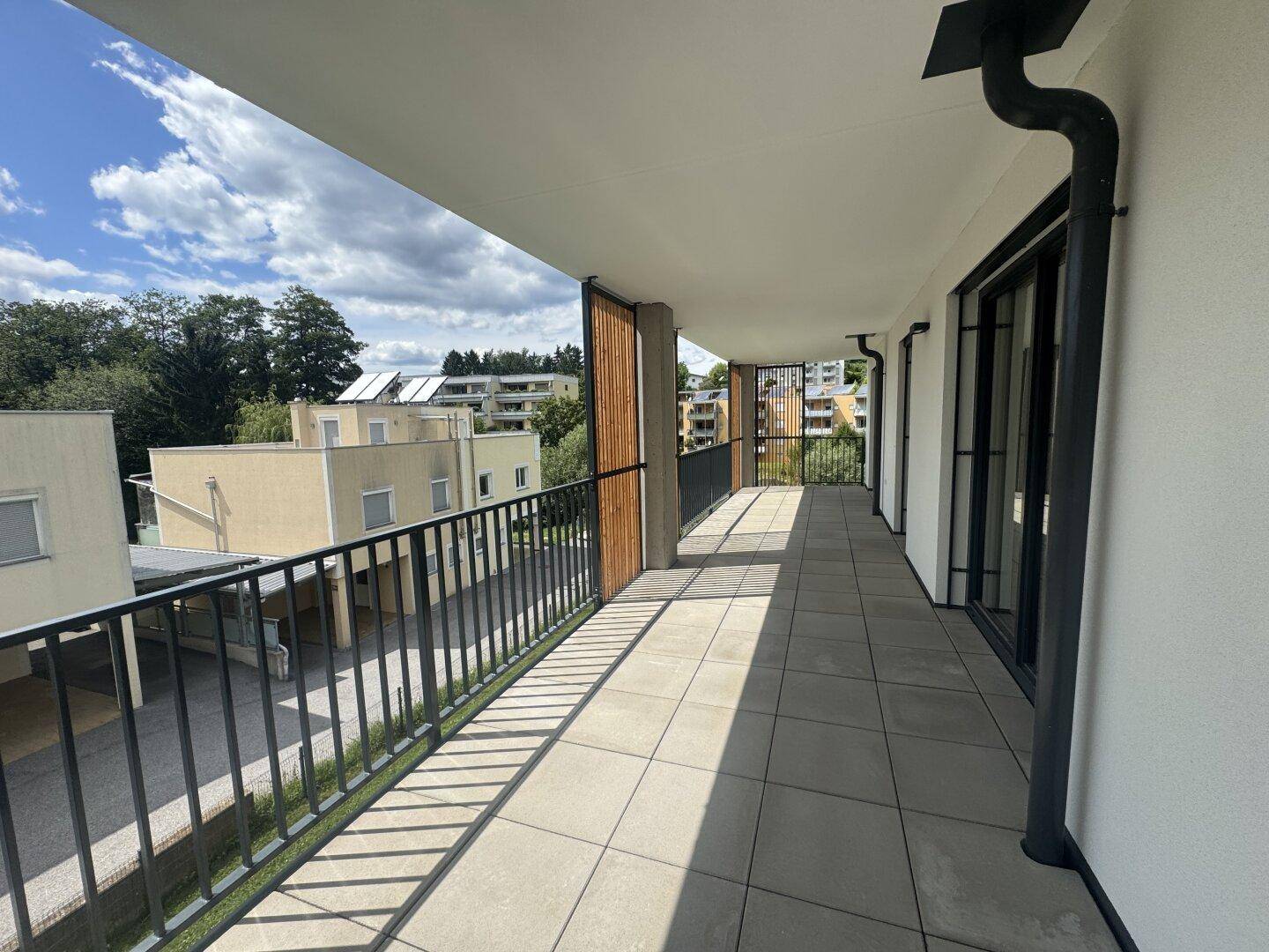 Geräumiger Balkon mit Fliesenboden und Blick auf die grüne Umgebung und benachbarte Gebäude.