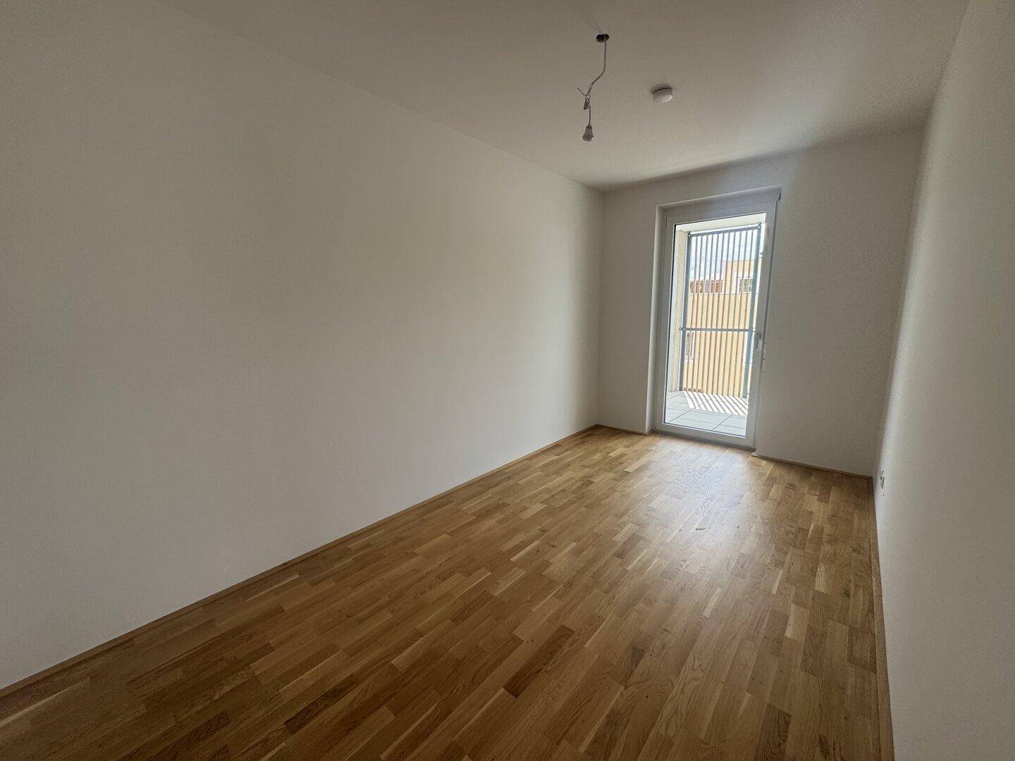 Helles Schlafzimmer mit Parkettboden und Zugang zu einem kleinen Balkon, ideal für frische Luft.