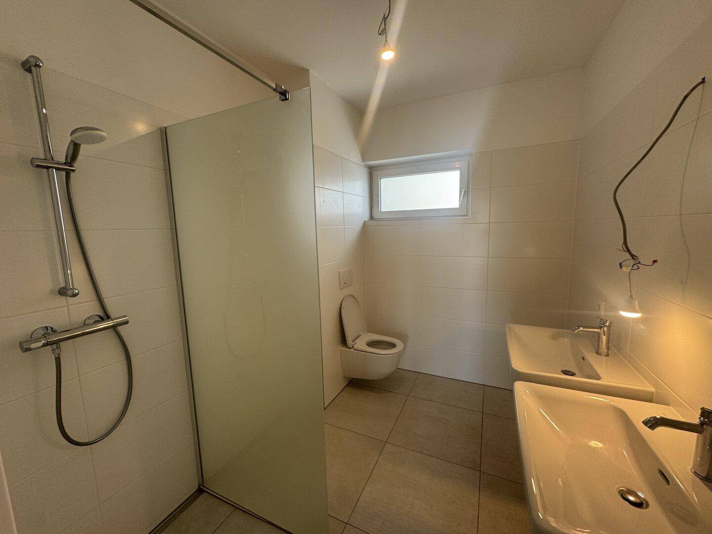 Modernes Badezimmer mit begehbarer Dusche, Doppelwaschbecken und einem Fenster für natürliche Belüftung.