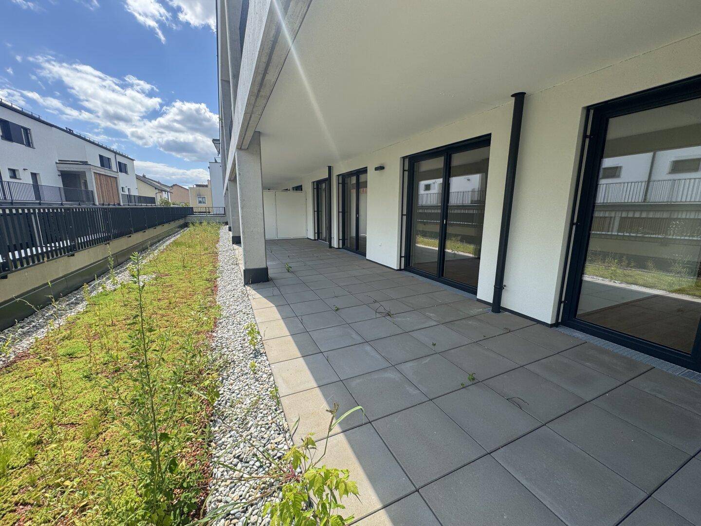 Große, gepflasterte Terrasse im Erdgeschoss mit Zugang zu einem begrünten Bereich.