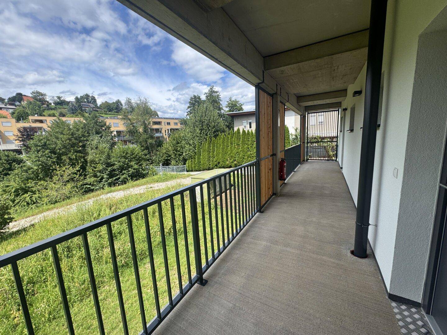 Überdachte Loggia mit schwarzem Geländer und weitem Blick ins Grüne.