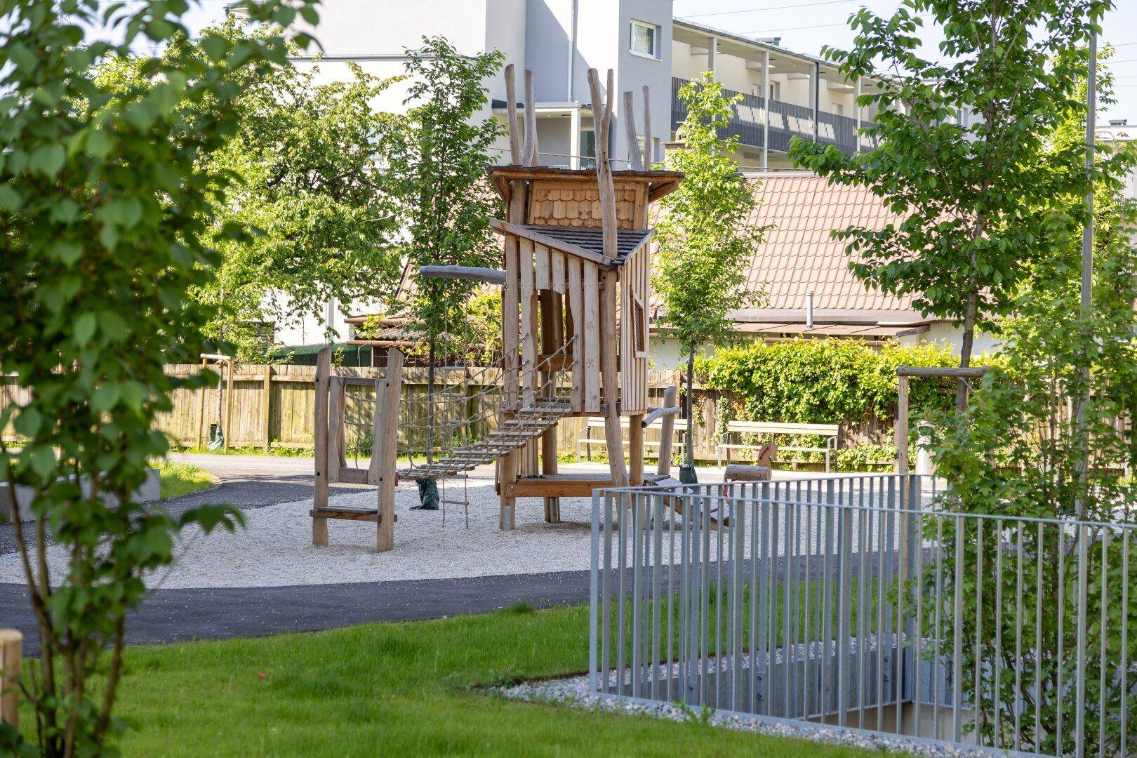 Detailansicht eines naturnahen Kinderspielplatzes mit Holzturm und Seilbrücke.