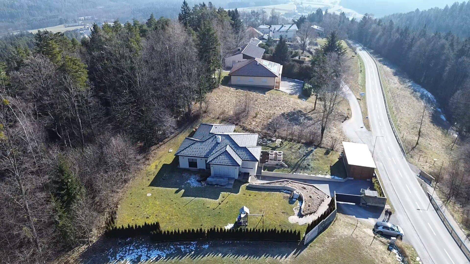 Luftaufnahme eines Einfamilienhauses mit Garten, Auffahrt und angrenzender Straße in ländlicher Umgebung.