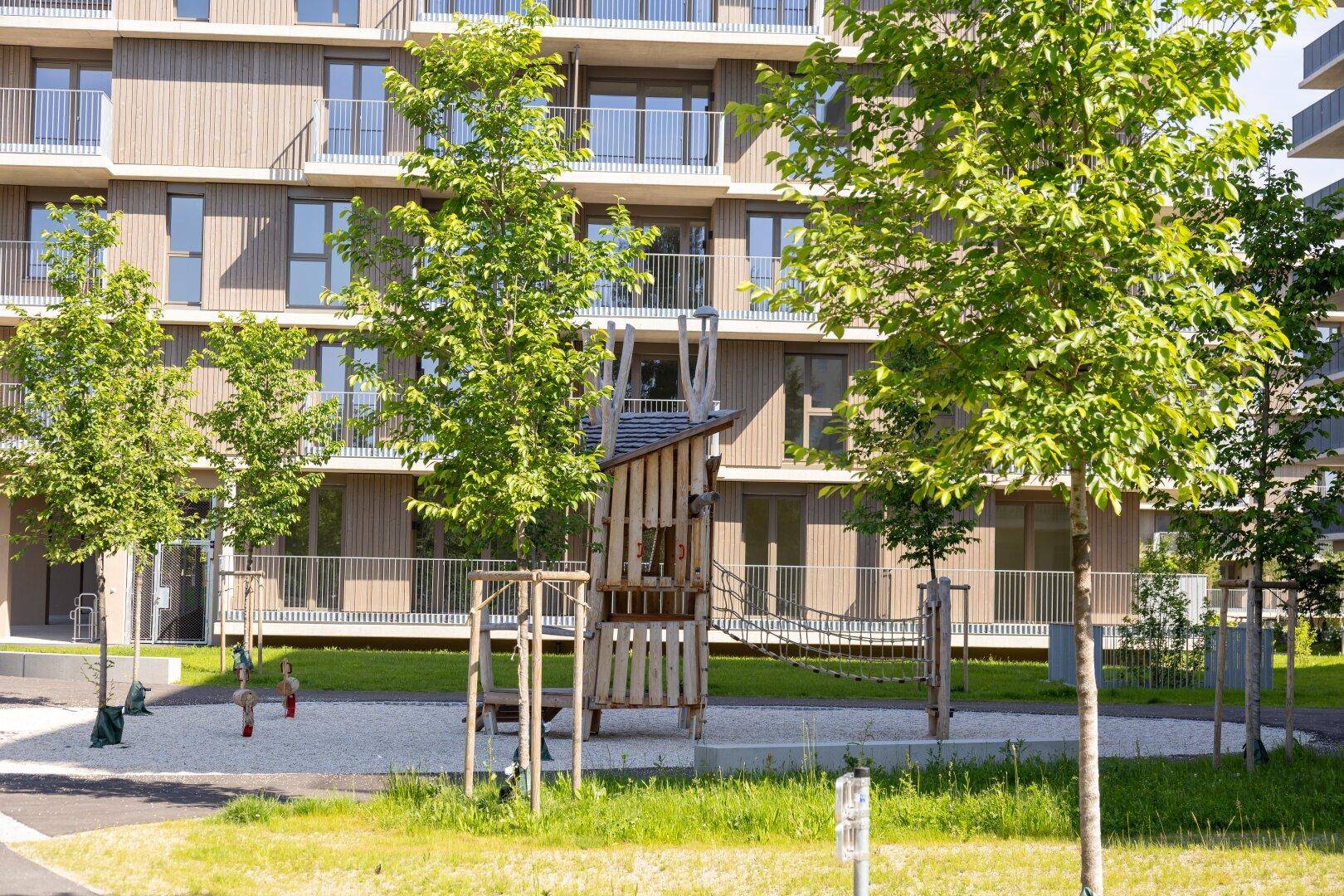 Ansicht des modernen Wohngebäudes mit Holzverkleidung und einem gut ausgestatteten Spielplatz im Vordergrund.