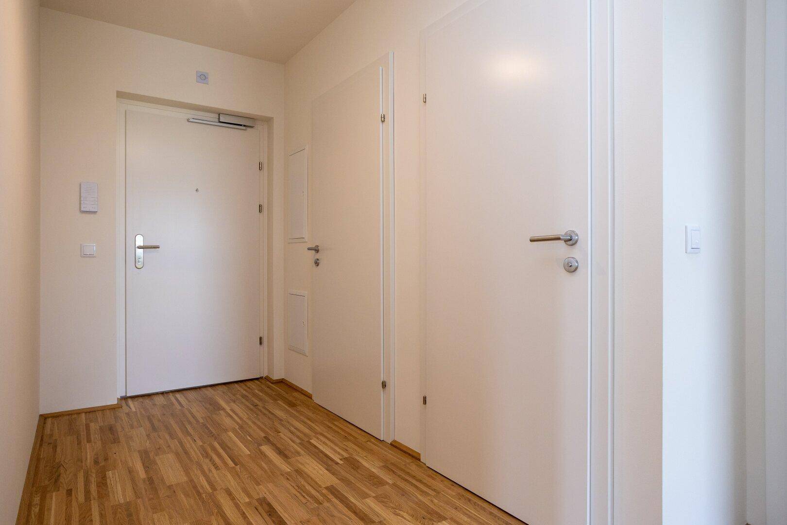 Heller Flur mit Holzboden und weißen Türen, der zu den verschiedenen Räumen der Wohnung führt.