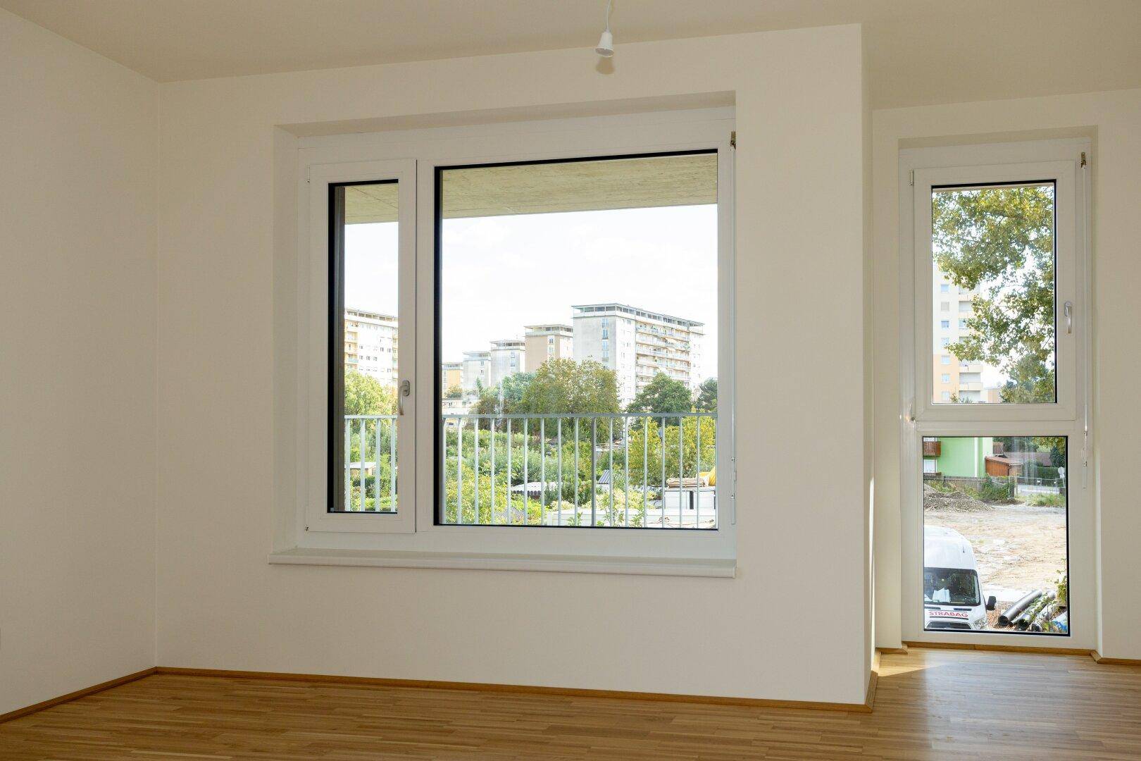 Große Fenster im Wohnzimmer bieten einen weiten Blick auf die grüne Umgebung und Stadtlandschaft.